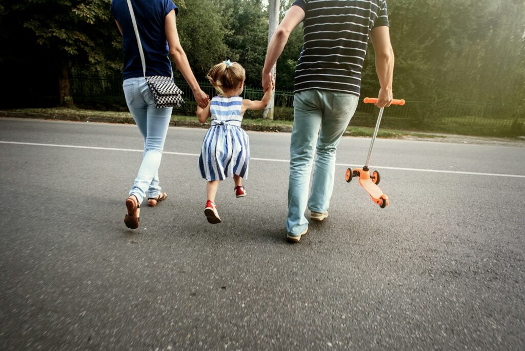 happy stylish parents holding hands with daughter and walking in sunny summer street